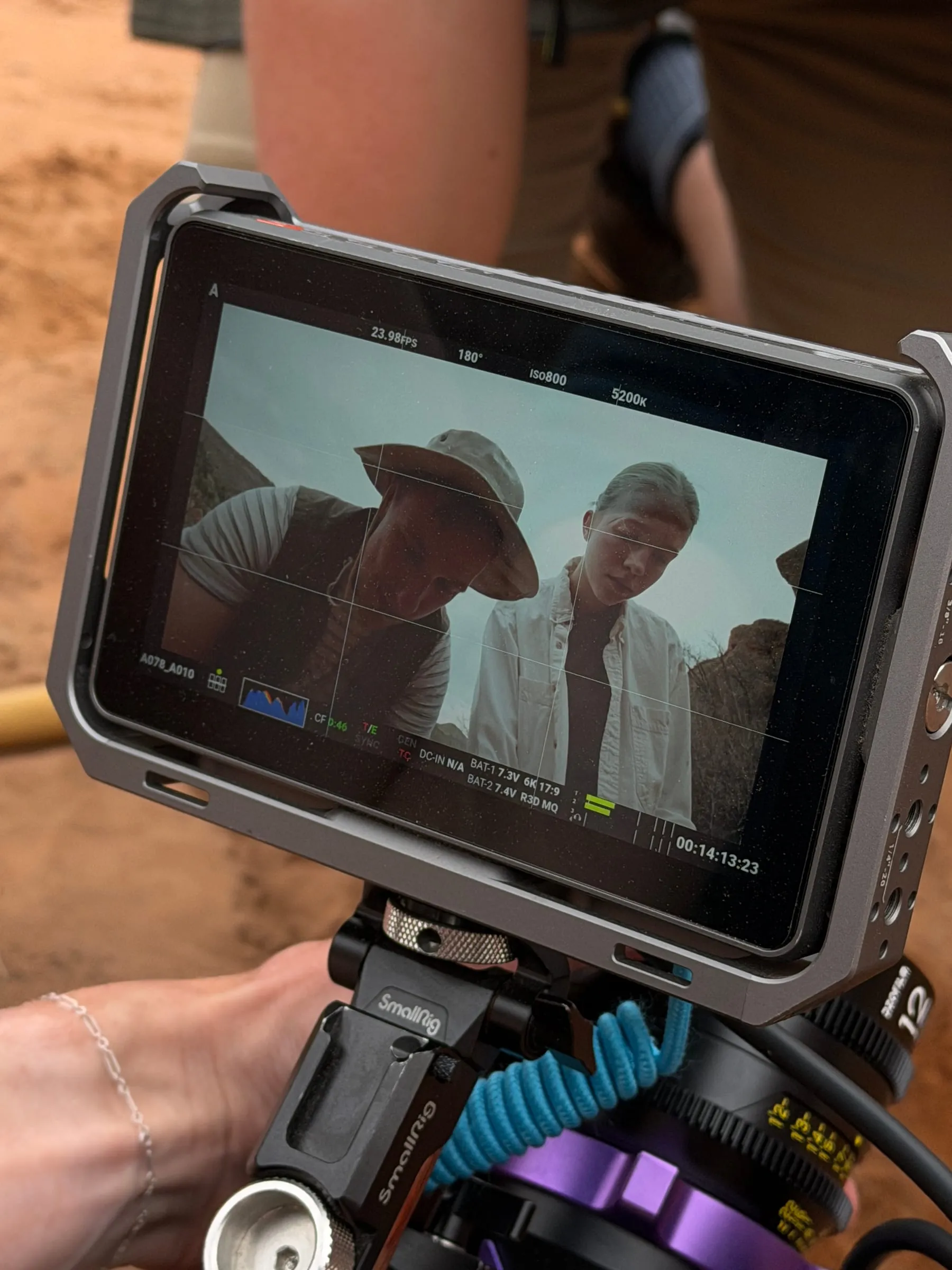 A handheld monitor shows the two actors in close-up, looking down into the dig