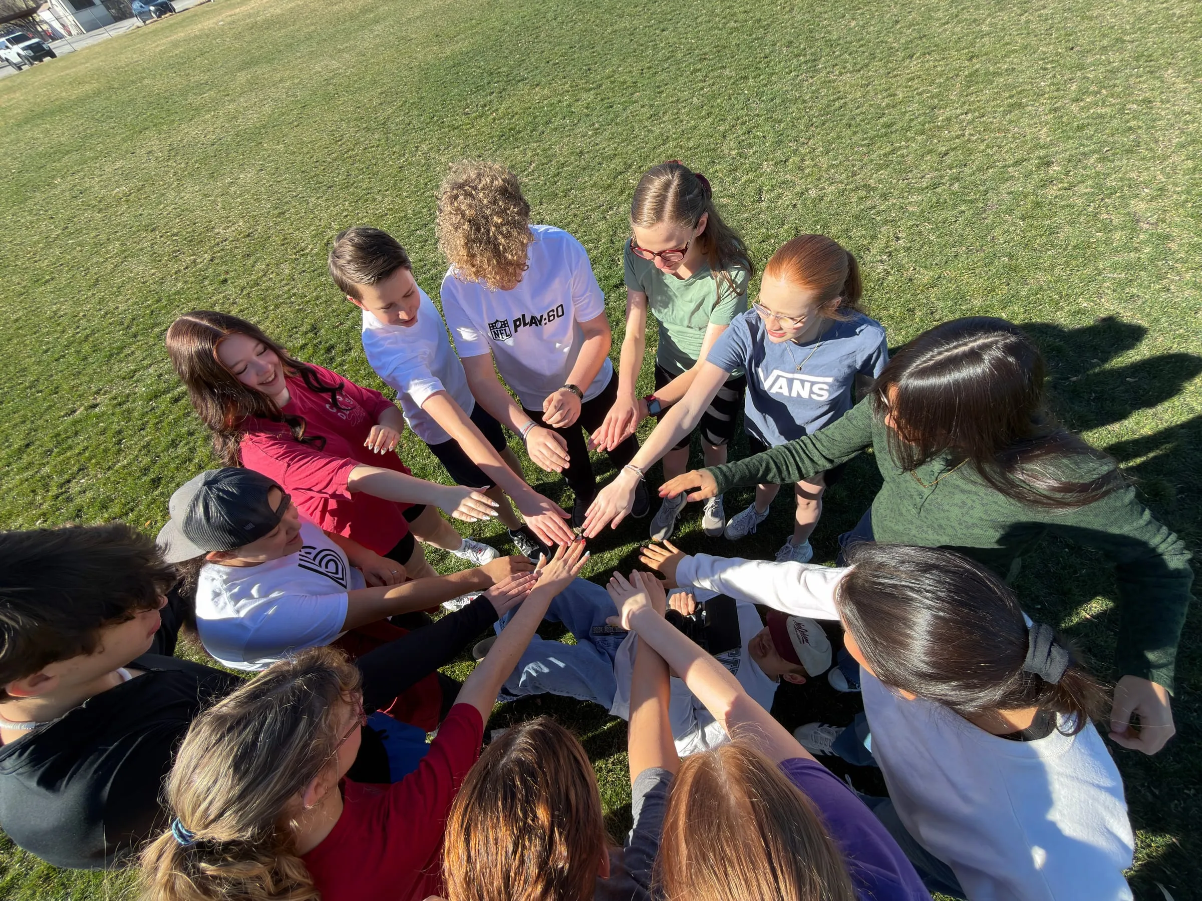 From above, a circle of teens in the grass stacks their hands in the middle