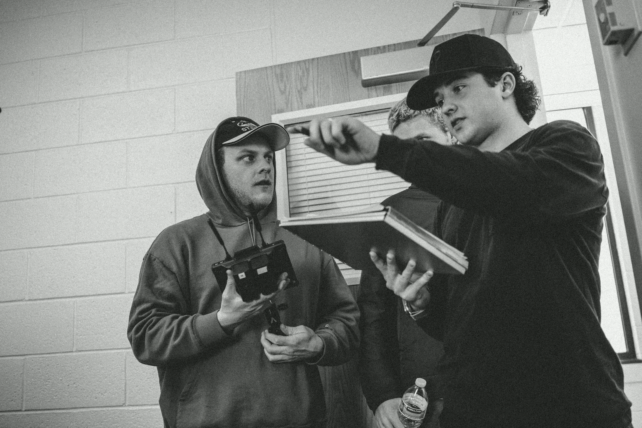 In black and white, a crew member points out a shot in a notebook while another holds a camera monitor