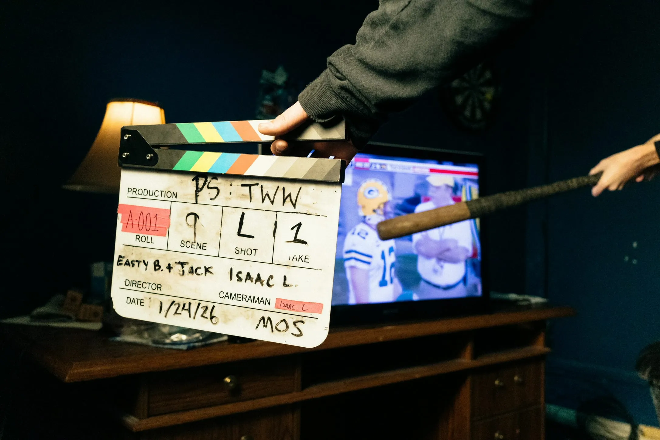 A slate for scene 9, dated 1/24/26, held up in front of a TV showing a football game