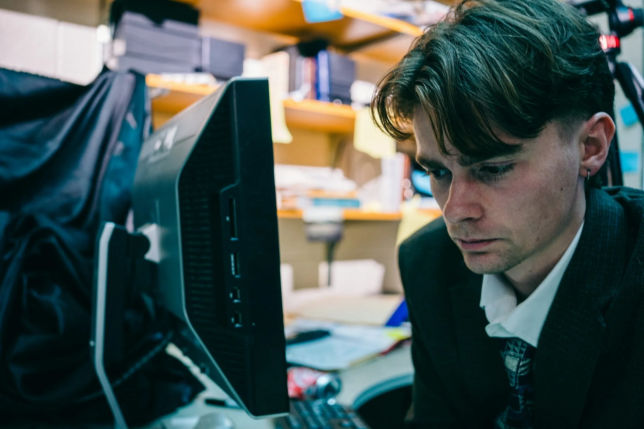 A young man in a suit and tie works at an office computer under a softbox