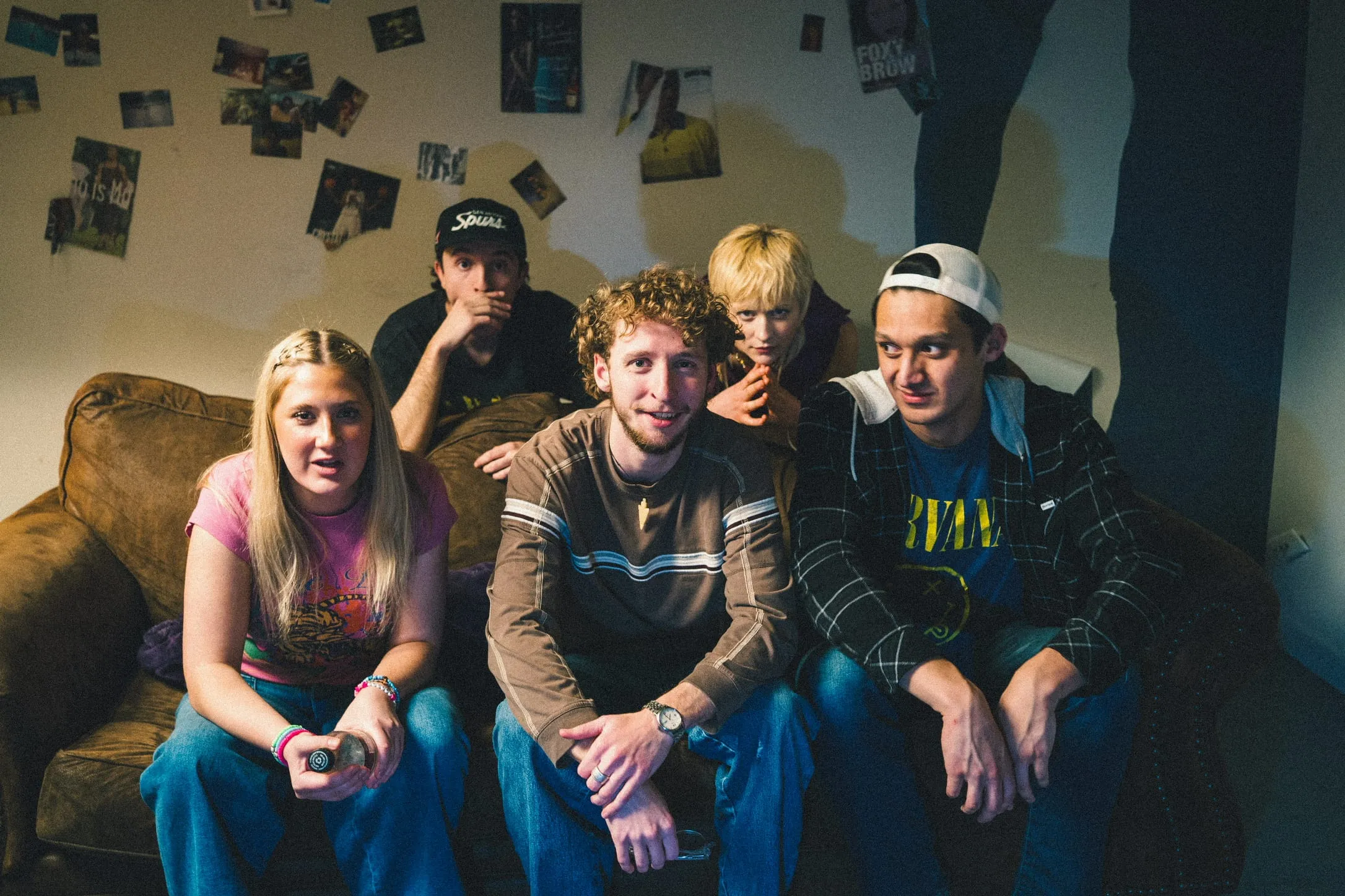 Five actors crowd onto the couch in the basement set, photos on the wall behind them