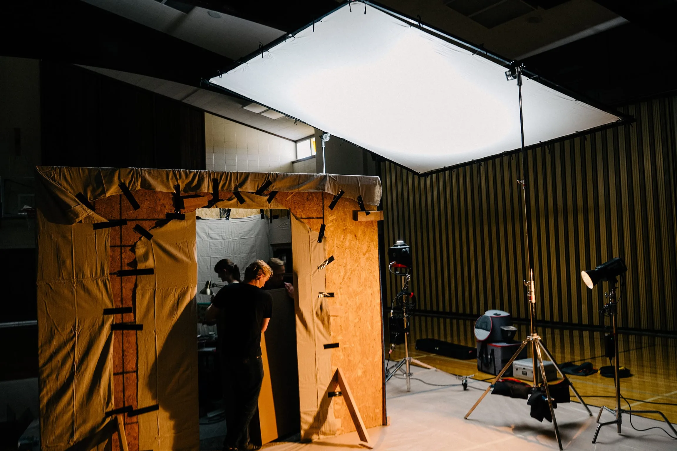 Inside a church cultural hall, the office set's wooden walls stand under a big overhead silk, lights on stands around it