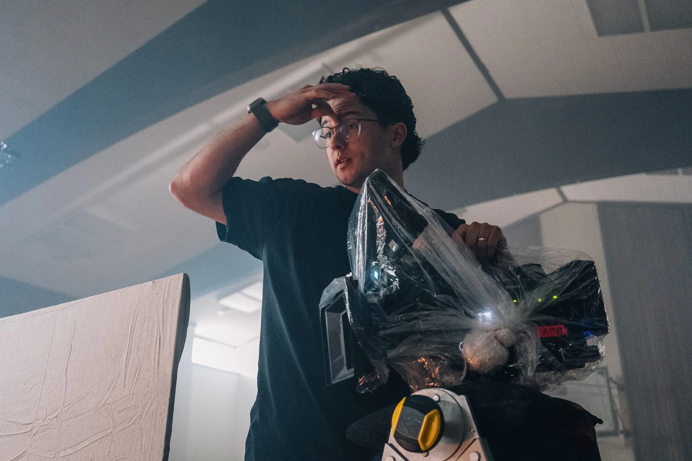 Under the hall's lights, a crew member shades his eyes while holding a camera wrapped in plastic