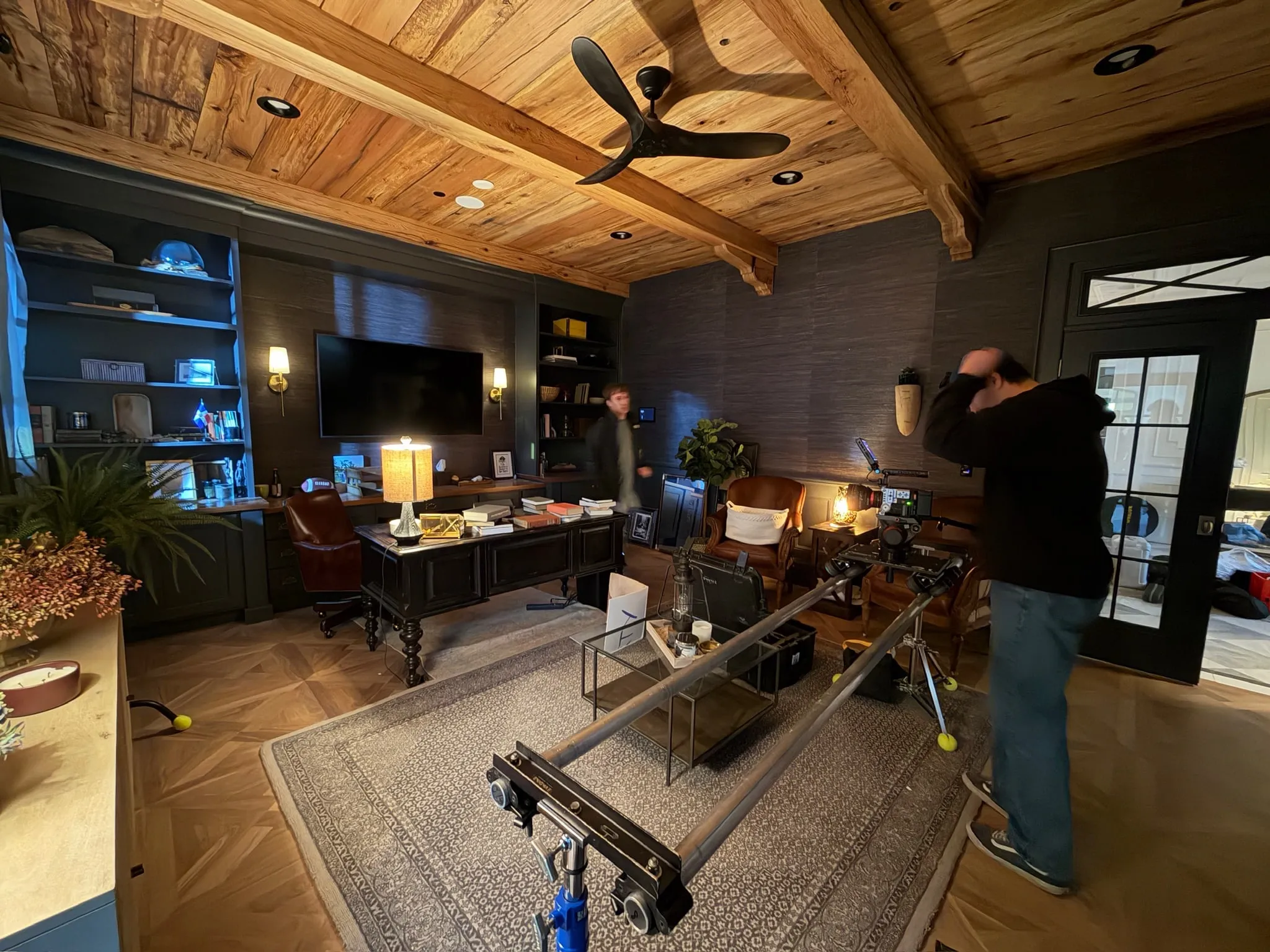 A wood-beamed study set up for a shot, a camera slider stretched across the rug toward the book-covered desk