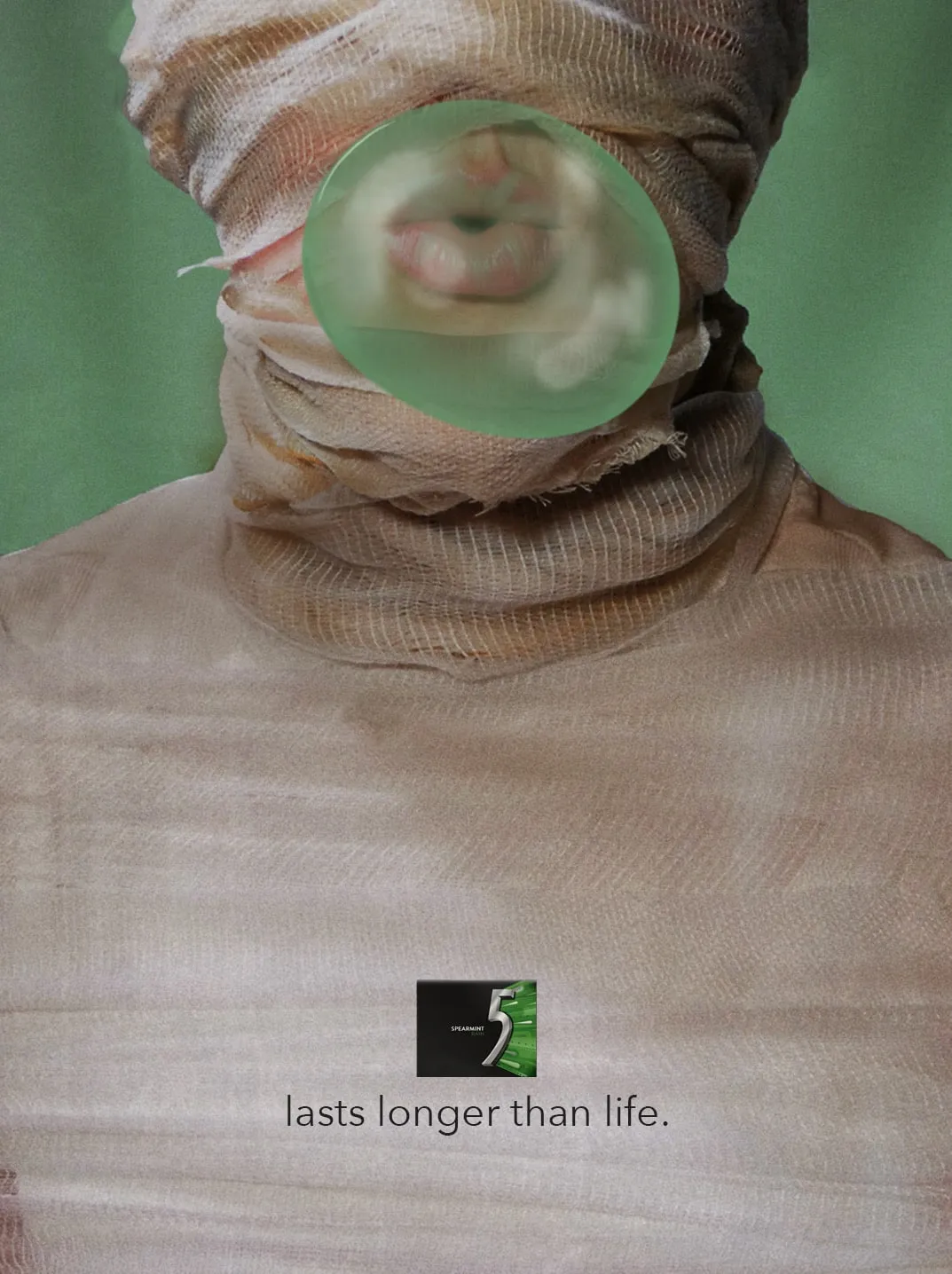 A mummy in gauze wrappings blows a green bubble through a gap at its mouth. Under a pack of 5 Spearmint Rain: “lasts longer than life.”