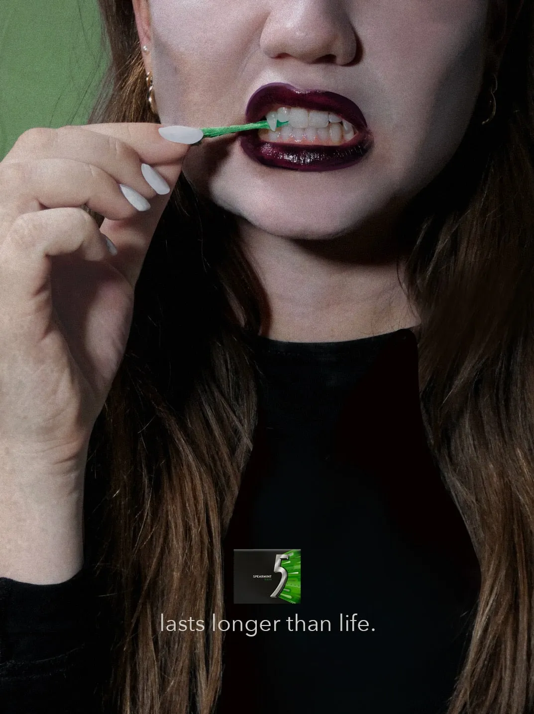 A vampire in dark lipstick pulls a strand of green gum from her fangs. Under a pack of 5 Spearmint Rain: “lasts longer than life.”