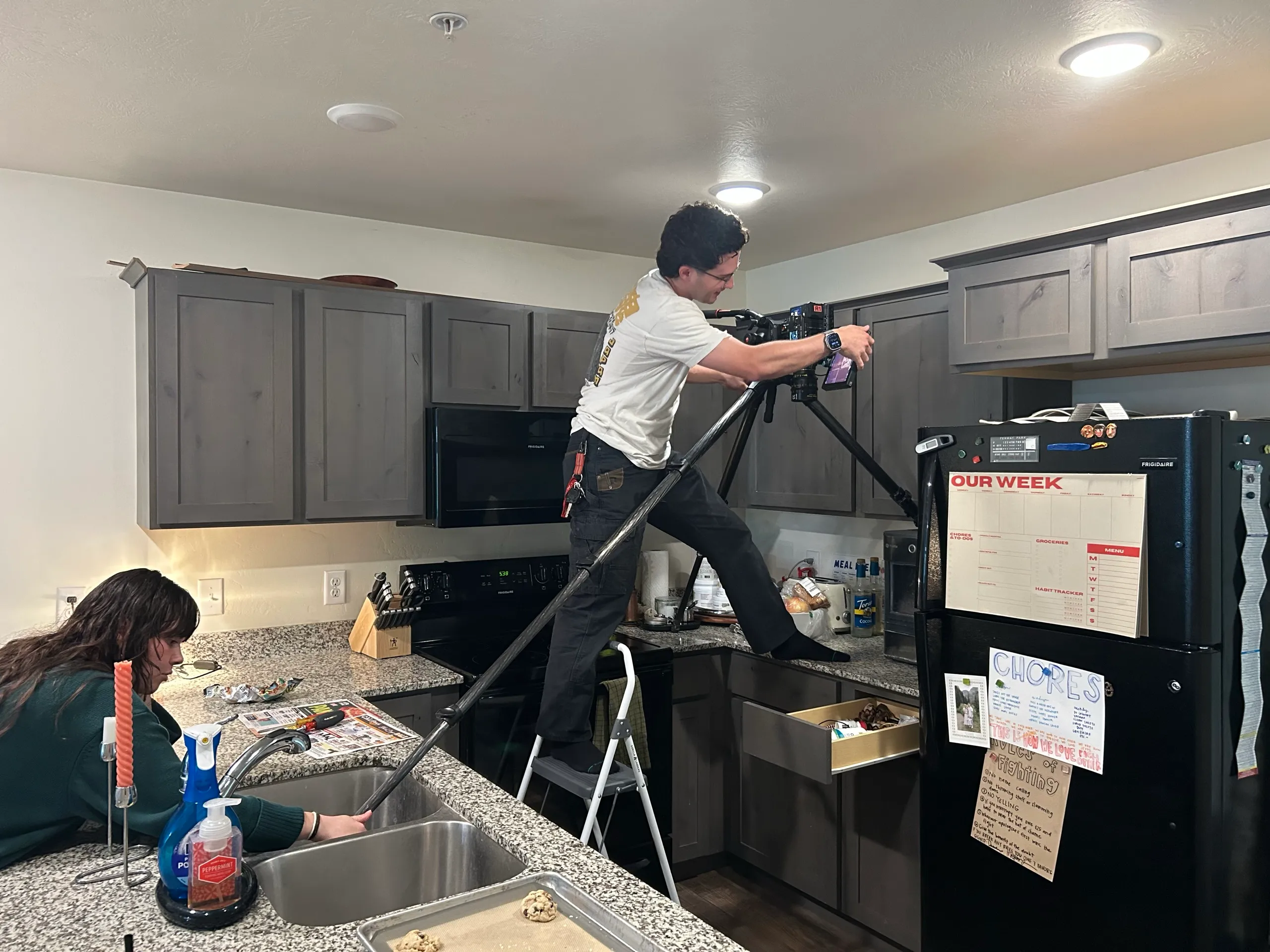 Behind the scenes: the tripod spread across a kitchen to shoot straight down into an open drawer, one leg in the sink with someone holding it, one in the toaster and one against the backsplash, the operator on a step stool