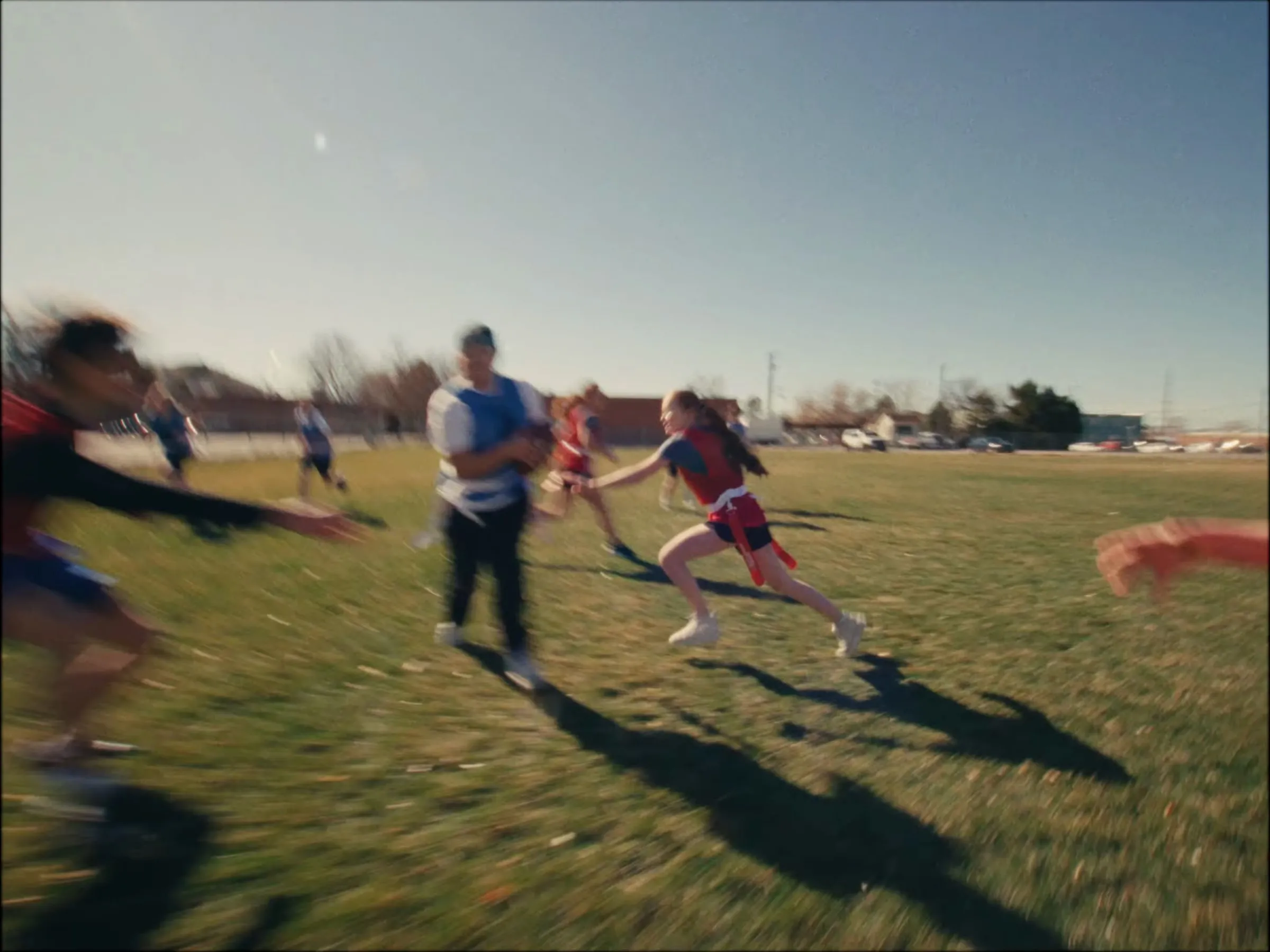 A flag football game in motion blur: a girl in a red pinnie reaches for the flag of a player carrying the ball