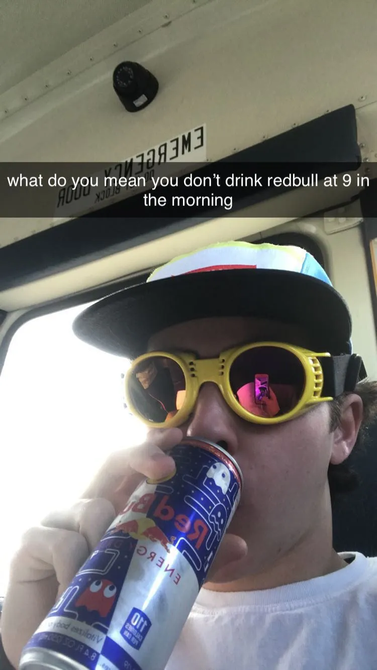 Tommy on a bus in yellow goggles and a flat-brim cap, drinking a Red Bull, captioned "what do you mean you don't drink redbull at 9 in the morning"