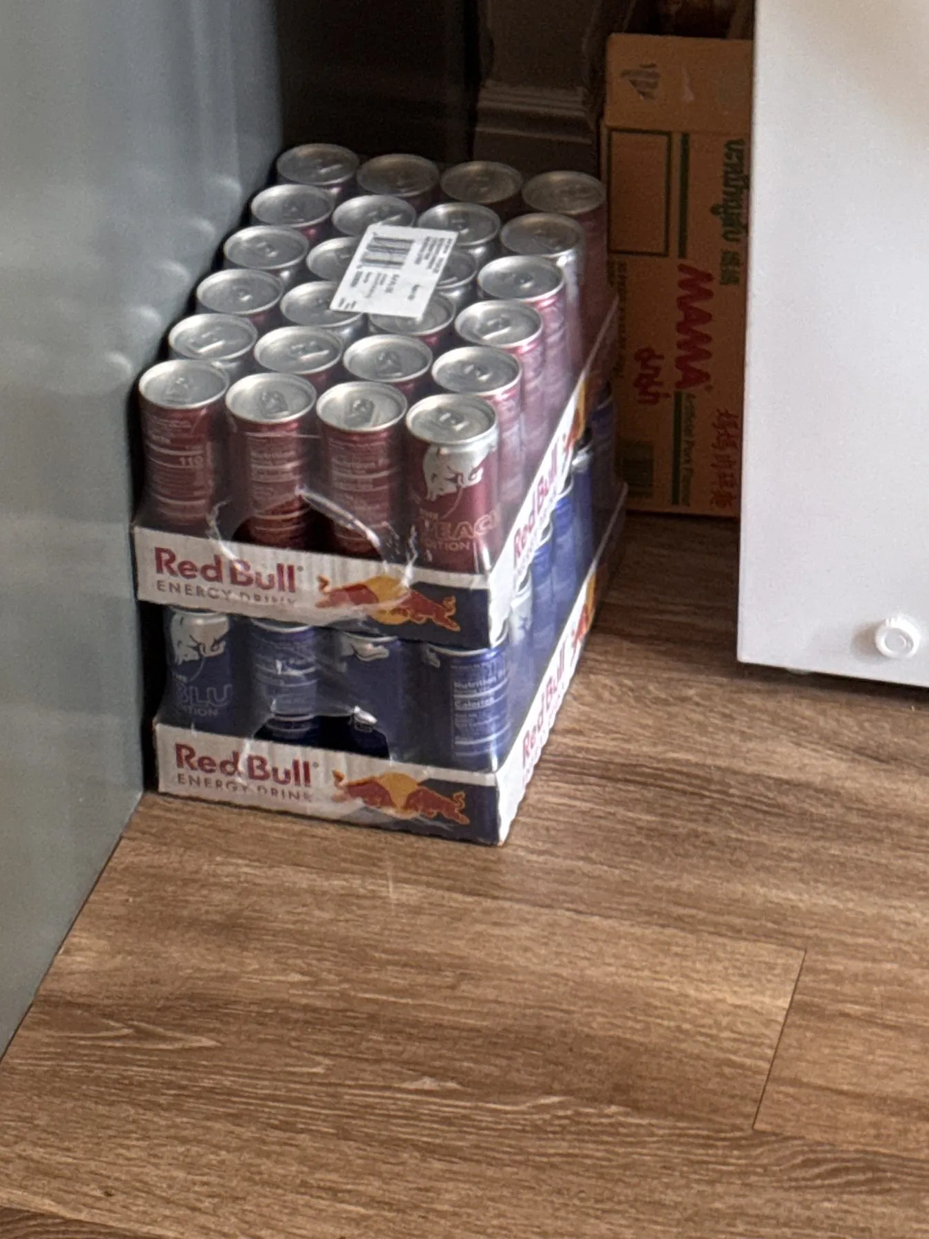 Two flats of Red Bull stacked in a corner, the Peach Edition on the Blue Edition