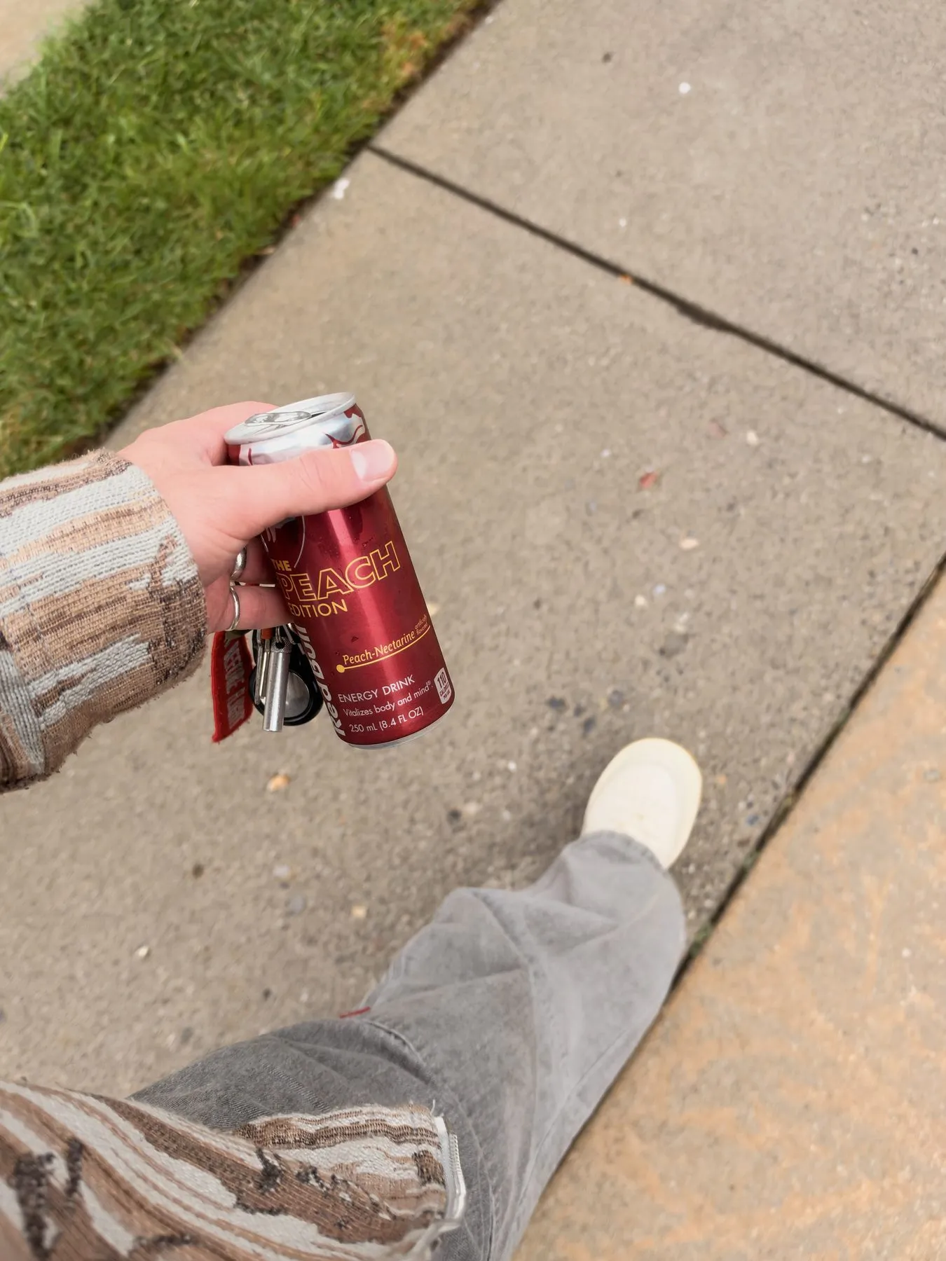 A Peach Edition can and a set of keys in hand, on a sidewalk