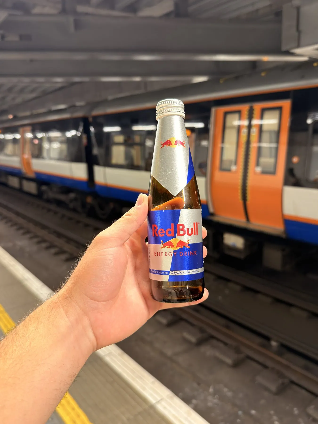 A glass bottle of Red Bull held up on a train platform in London