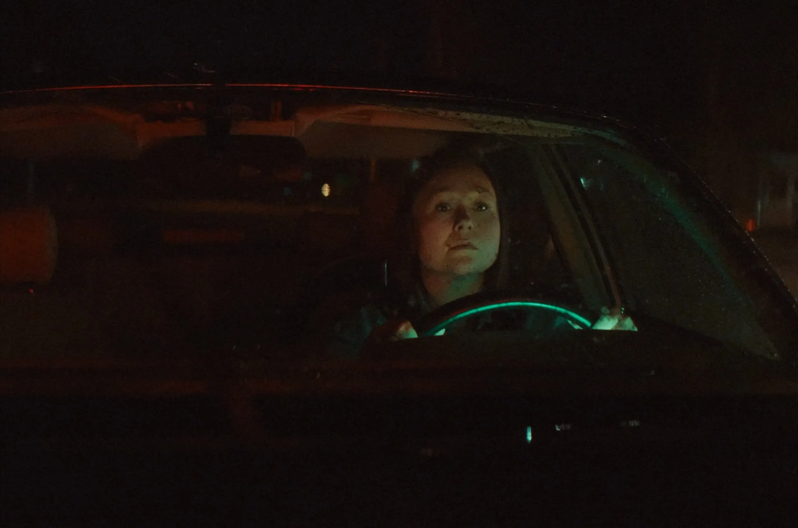A woman drives at night, lit by the dashboard