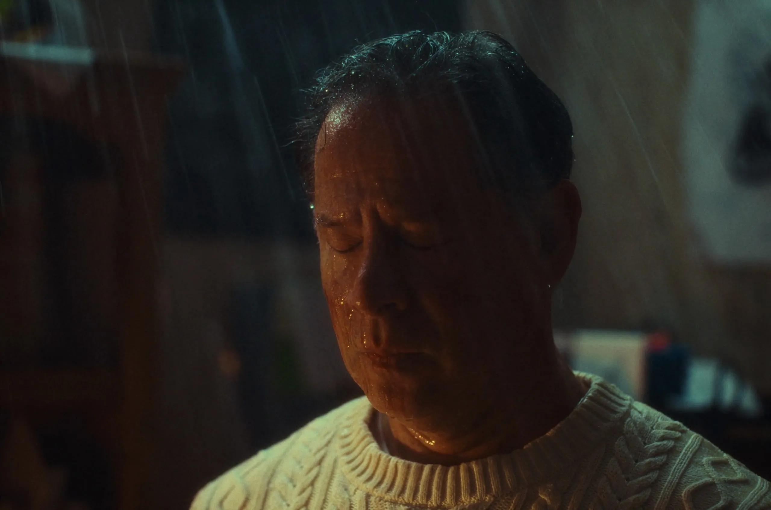 A man in a white sweater, eyes closed, in the rain